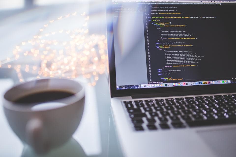 A laptop showing code next to a cup of coffee
